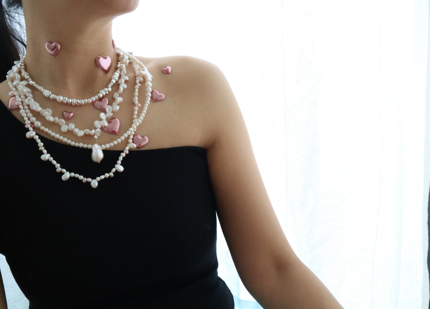 Woman wearing a pearl necklace with pink heart-shaped pendants against a white background